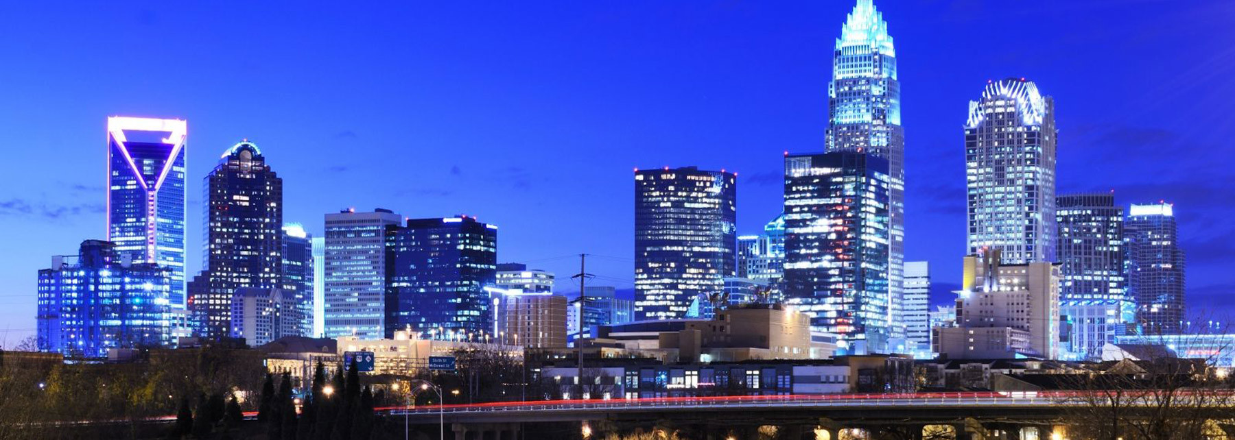 Night cityscape with brightly lit skyscrapers and modern office buildings against a blue sky